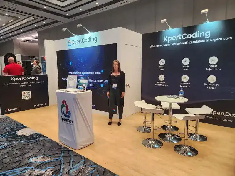 XpertDox booth at UCC 2023 showcasing XpertCoding, the AI medical coding solution, with a representative and attendees in a conference hall.